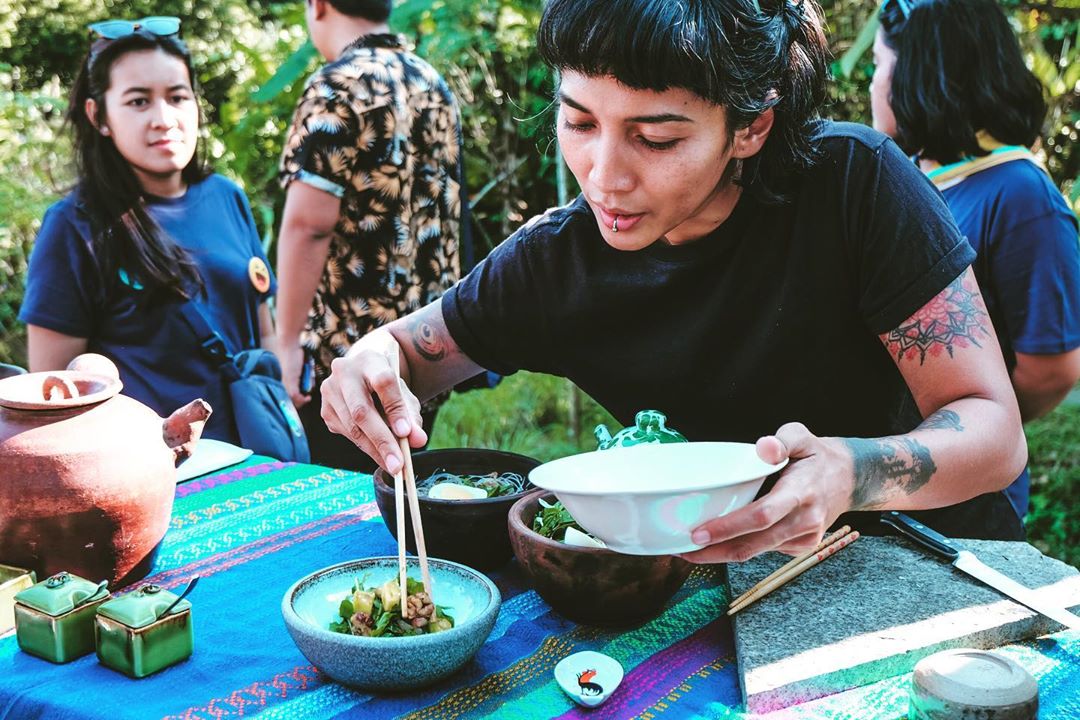 Ade sedang mengambil makanan menggunakan sumpit, hendak ditaruh di dalam mangkuknya.
