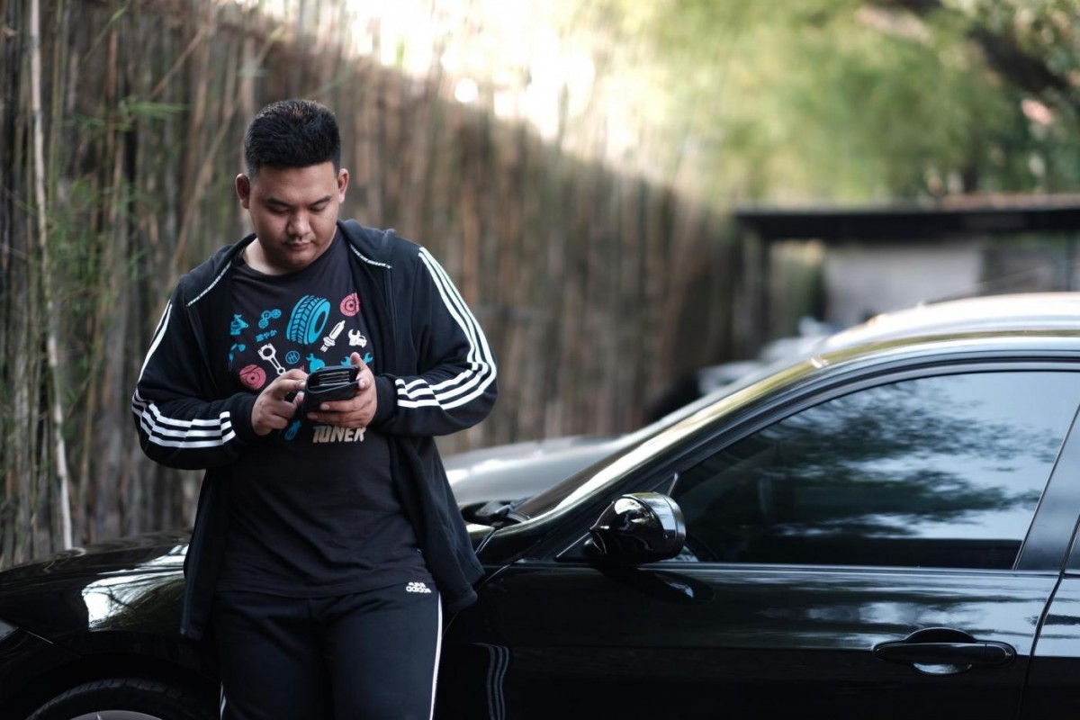 Evan Pratama sedang menggunakan handphone bersender pada mobil hitam