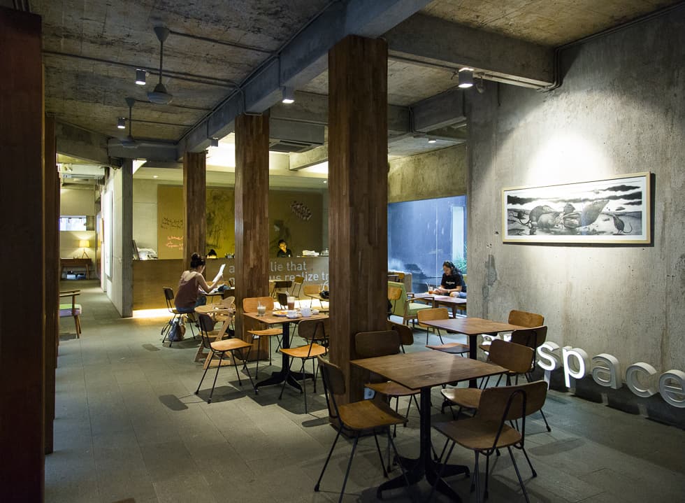 Tampilan indoor area Dia.Lo.Gue Cafe dengan meja dan kursi kayu serta dinding abu-abu