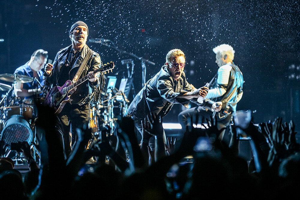 Bono, larry Mullen Jr, Adam Clayton dan The Edge saat Tur Joshua Tree Anniversary sedang menyiramkan minuman di botol pada penonton